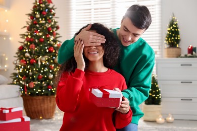 Photo of Happy man surprising his girlfriend with Christmas gift at home