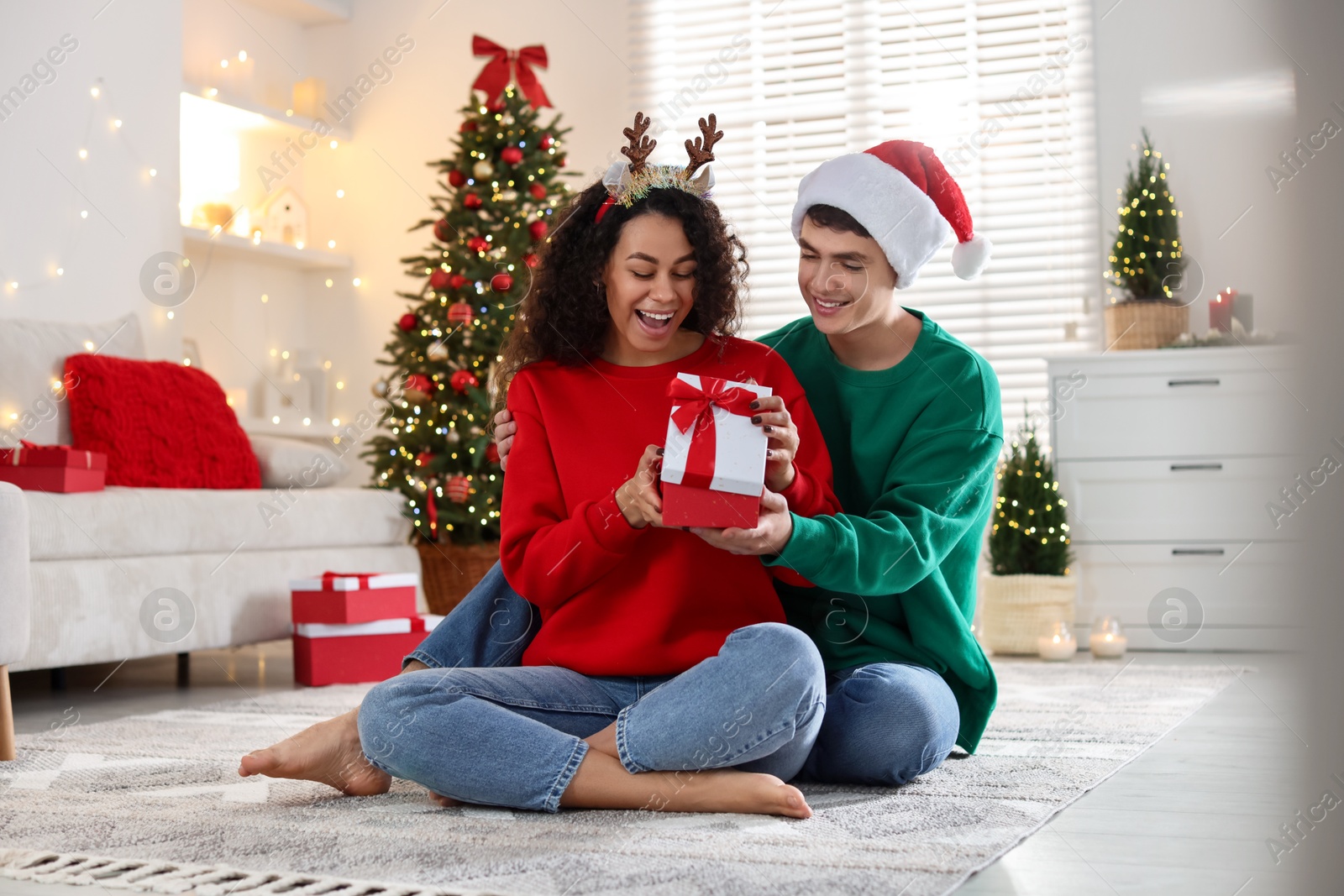 Photo of Young man giving Christmas gift to his happy girlfriend at home