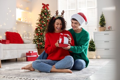 Photo of Young man giving Christmas gift to his happy girlfriend at home