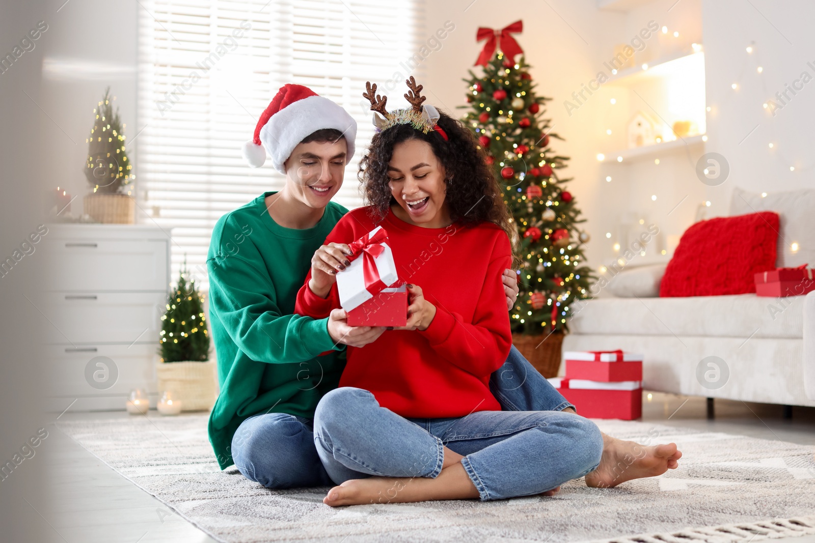 Photo of Young man giving Christmas gift to his happy girlfriend at home