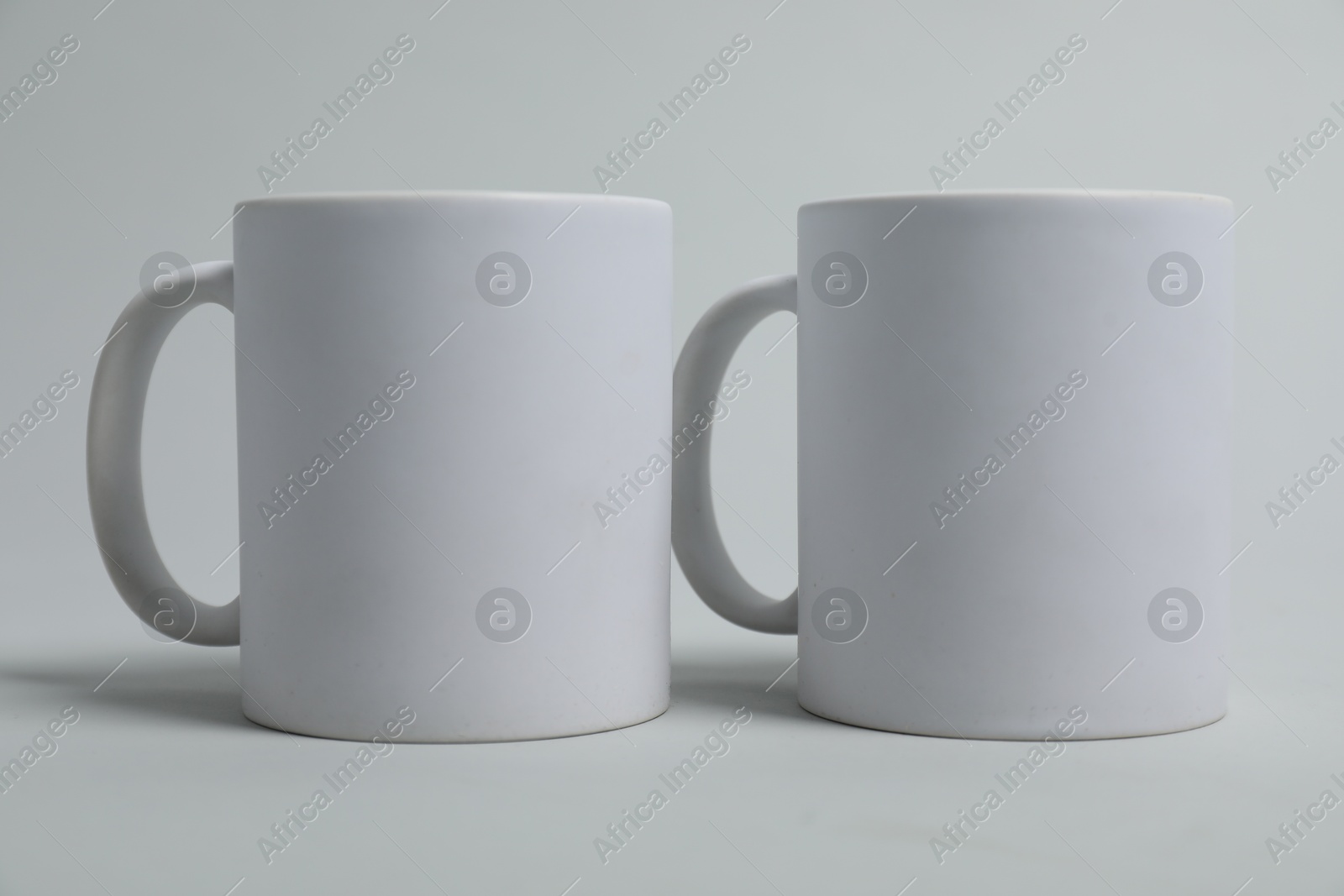 Photo of Two blank mugs for branding on light grey background. Mockup for design