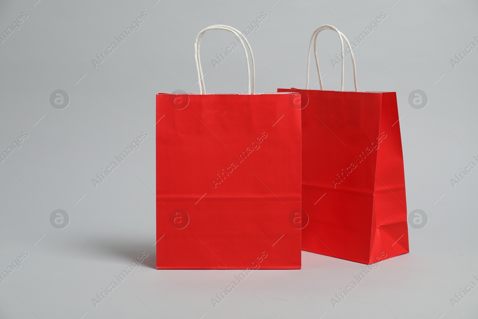 Photo of Two blank red shopping bags on light grey background. Mockup for design