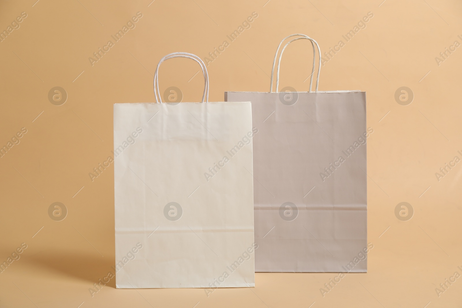 Photo of Two blank shopping bags on beige background. Mockup for design