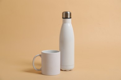 Photo of Blank mug and thermo bottle for branding on beige background. Mockup for design