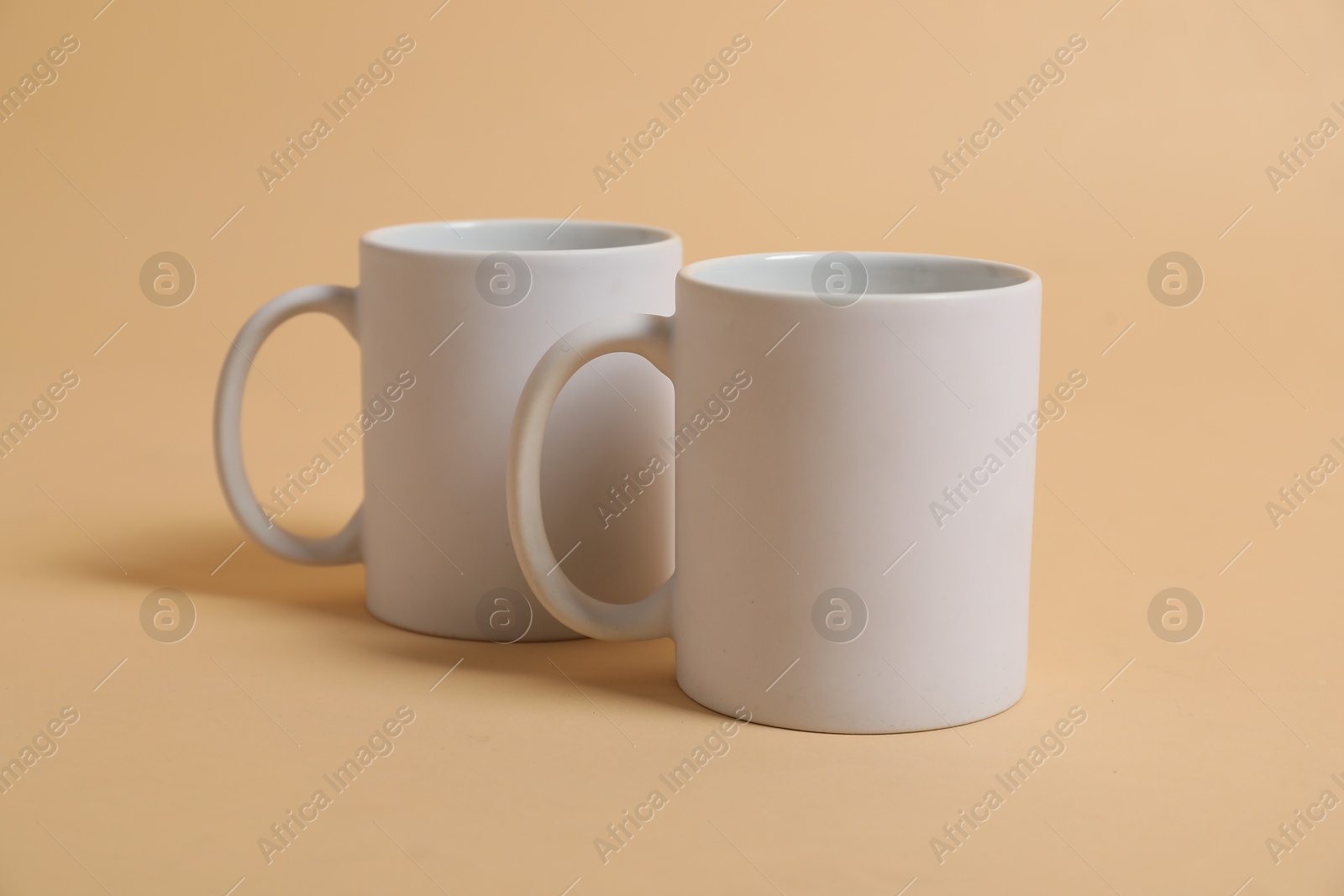 Photo of Two blank mugs for branding on beige background. Mockup for design