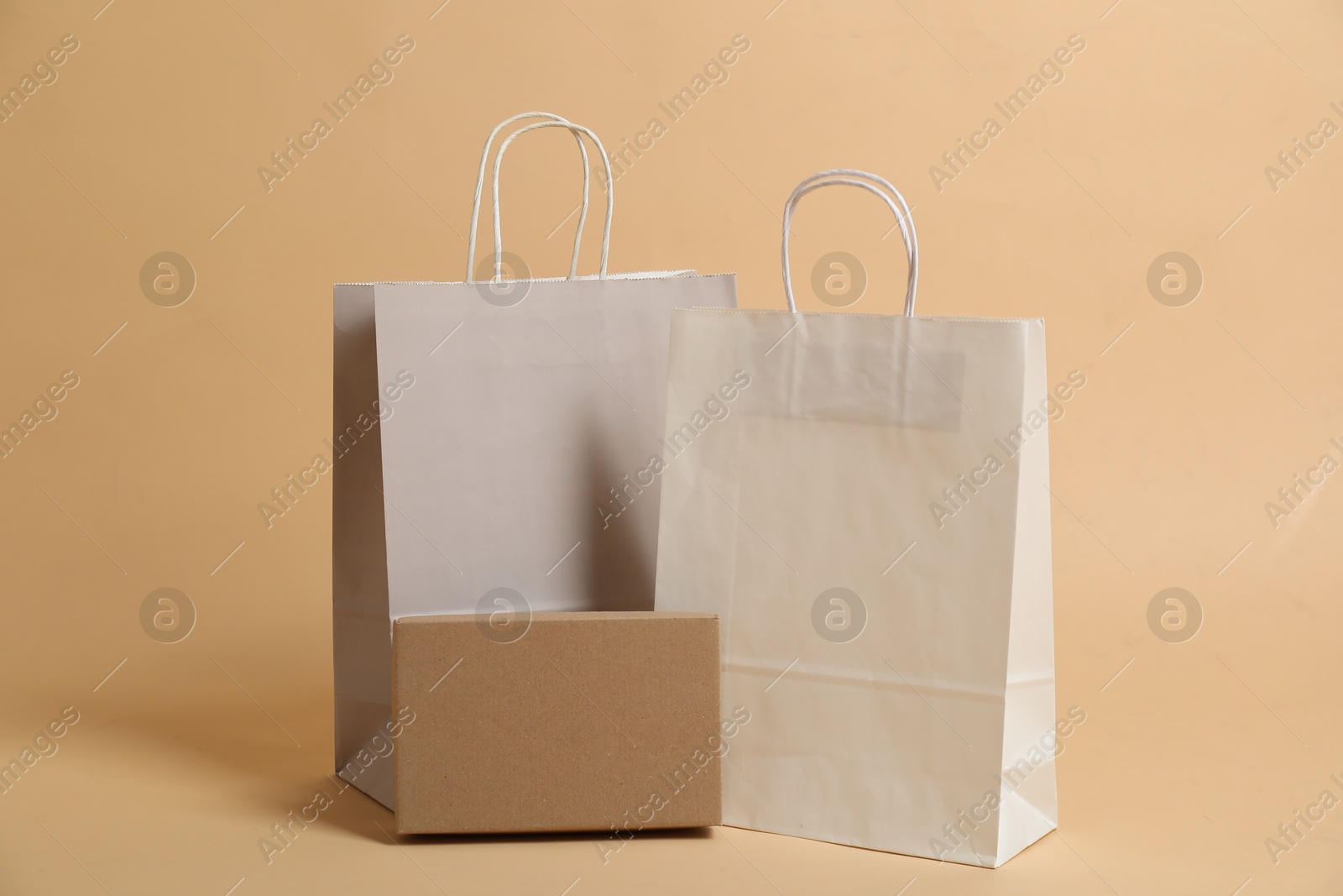 Photo of Blank shopping bags and cardboard box for branding on beige background. Mockup for design