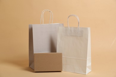 Photo of Blank shopping bags and cardboard box for branding on beige background. Mockup for design