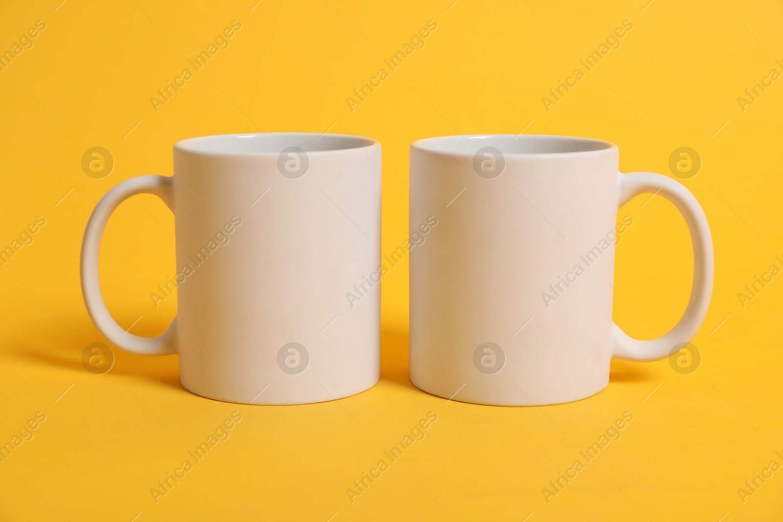 Photo of Two blank mugs for branding on orange background. Mockup for design