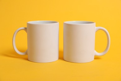 Photo of Two blank mugs for branding on orange background. Mockup for design