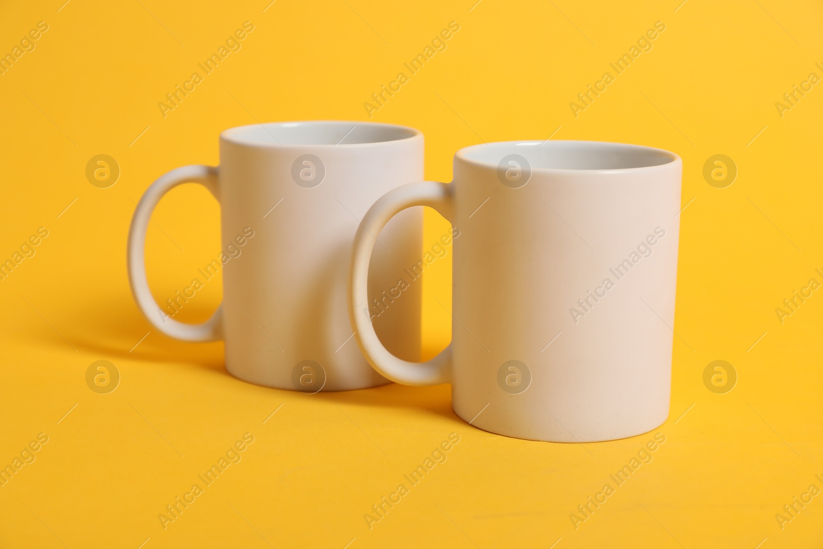 Photo of Two blank mugs for branding on orange background. Mockup for design