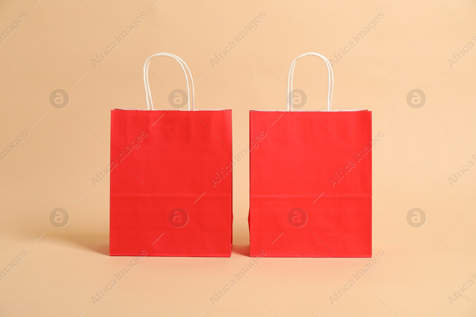 Photo of Two blank red shopping bags on beige background. Mockup for design