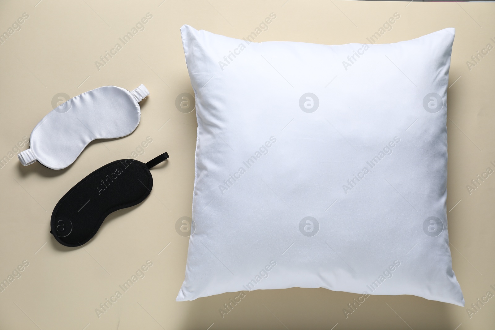 Photo of Blank white pillow and sleeping masks on beige background, flat lay. Mockup for design