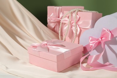 Photo of Beautiful wedding gifts, pearl jewelry and silk fabric on table against olive background