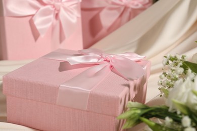 Photo of Beautiful wedding gifts, silk fabric and flowers on table, closeup