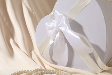 Photo of Beautiful wedding gift and pearl jewelry on silk fabric, closeup. Space for text