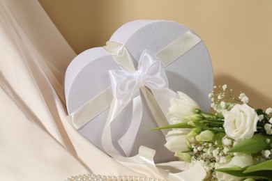 Photo of Beautiful wedding gift, pearl jewelry, flowers and silk fabric on beige background