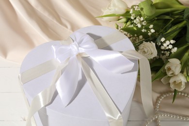 Photo of Beautiful wedding gift, pearl jewelry, flowers and silk fabric on white wooden table, closeup