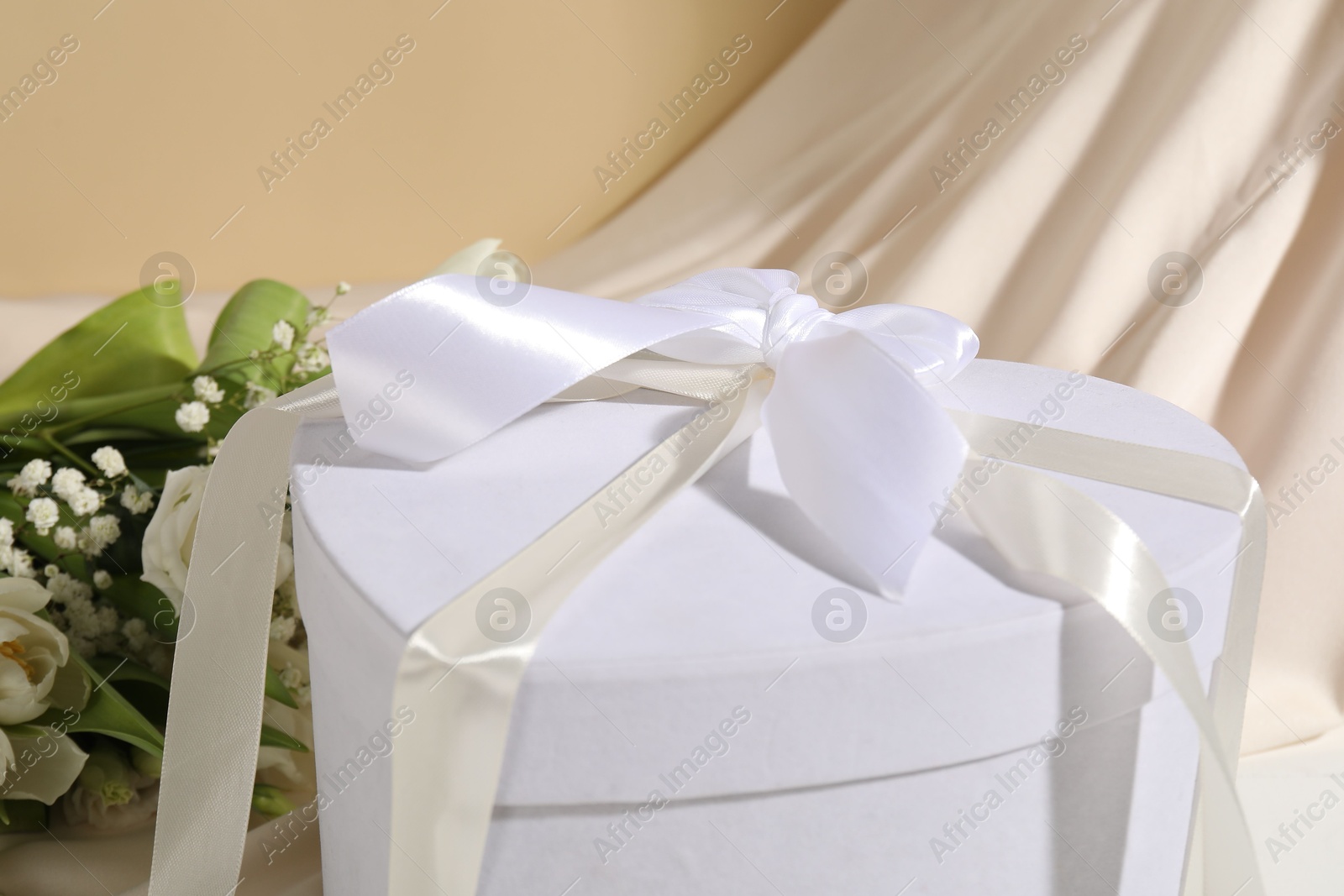 Photo of Beautiful wedding gift, flowers and silk fabric on beige background, closeup