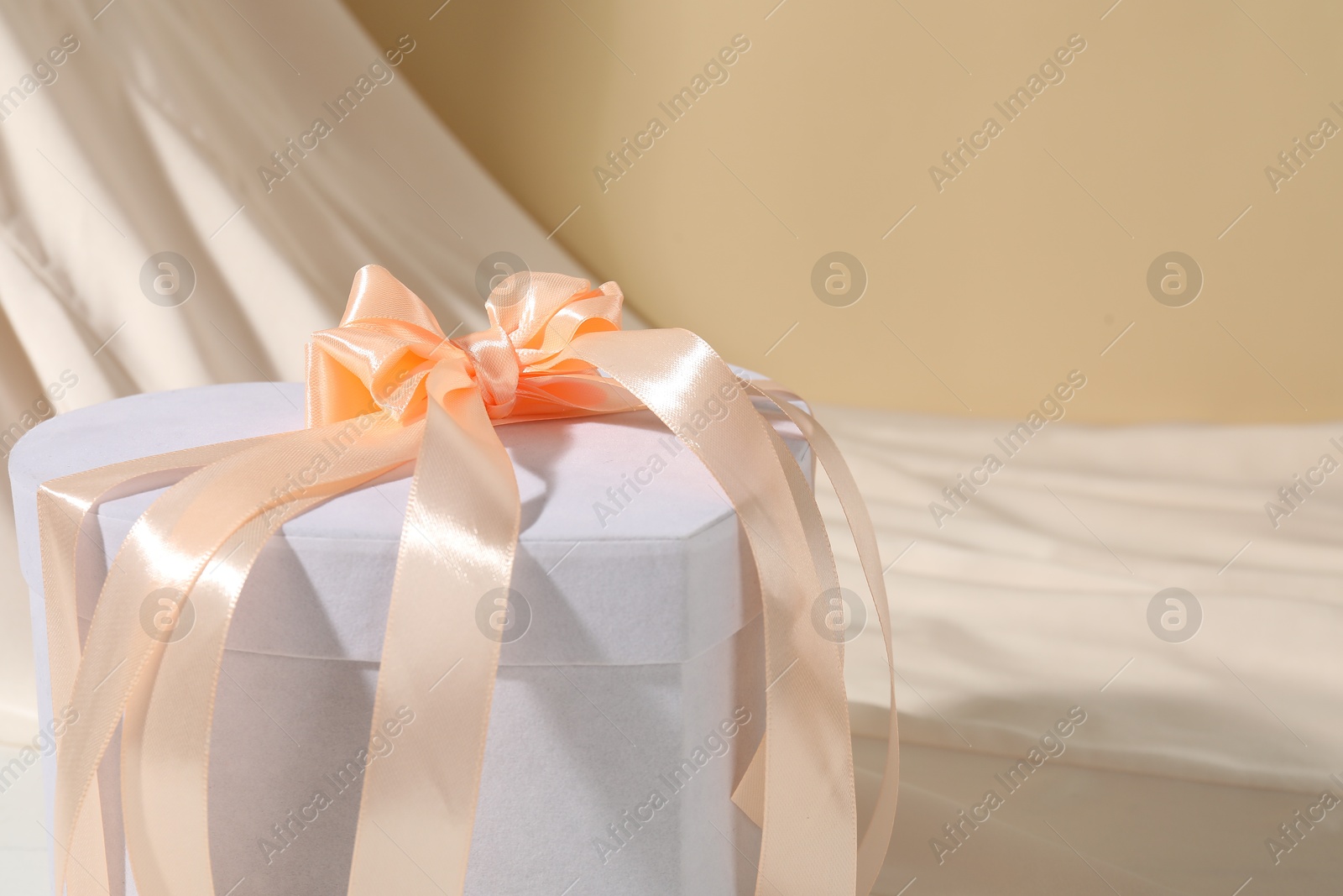 Photo of Beautiful wedding gift and silk fabric on beige background, closeup. Space for text