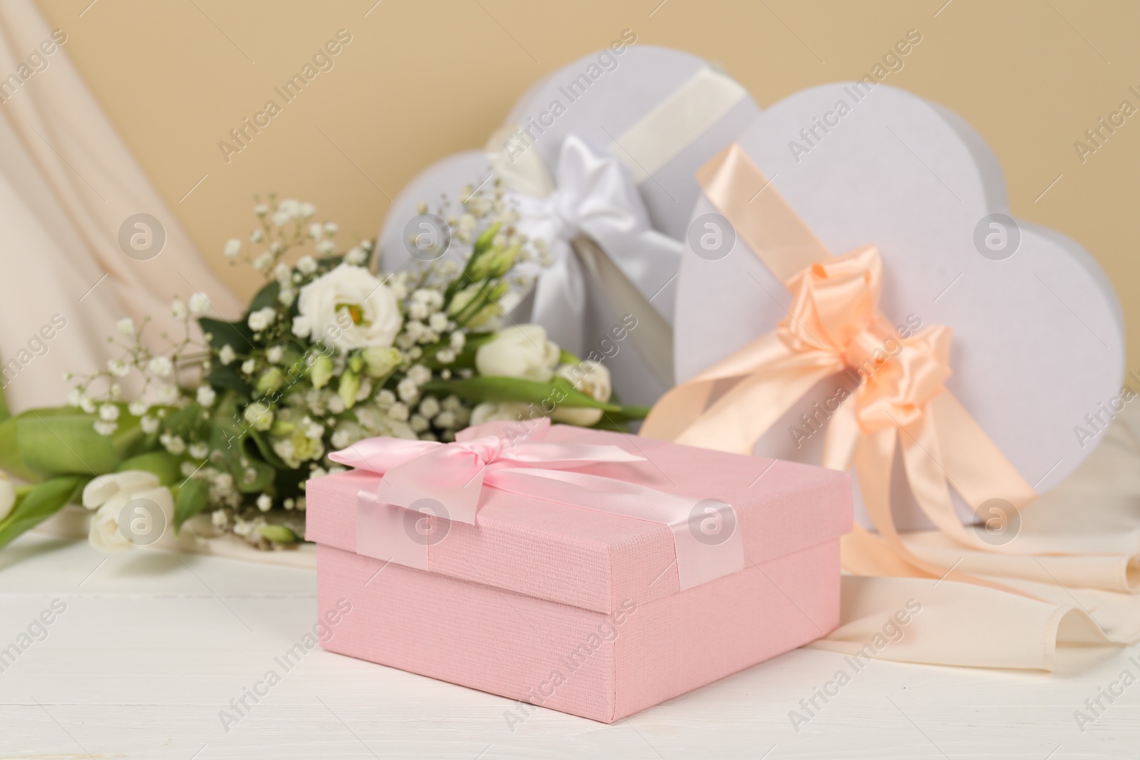 Photo of Beautiful wedding gifts, flowers and silk fabric on white wooden table, closeup