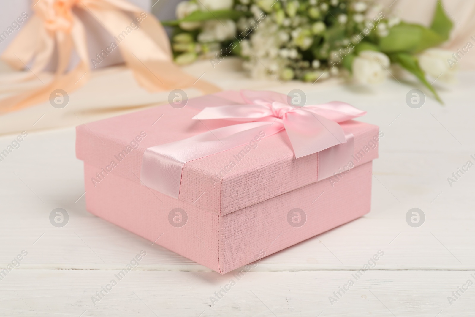 Photo of Beautiful wedding gift and flowers on white wooden table, closeup