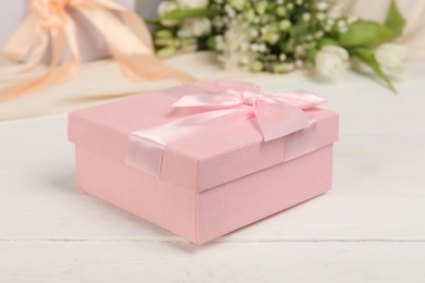 Photo of Beautiful wedding gift and flowers on white wooden table, closeup