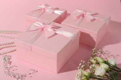 Photo of Beautiful wedding gifts, pearl jewelry and flowers on pink background, closeup