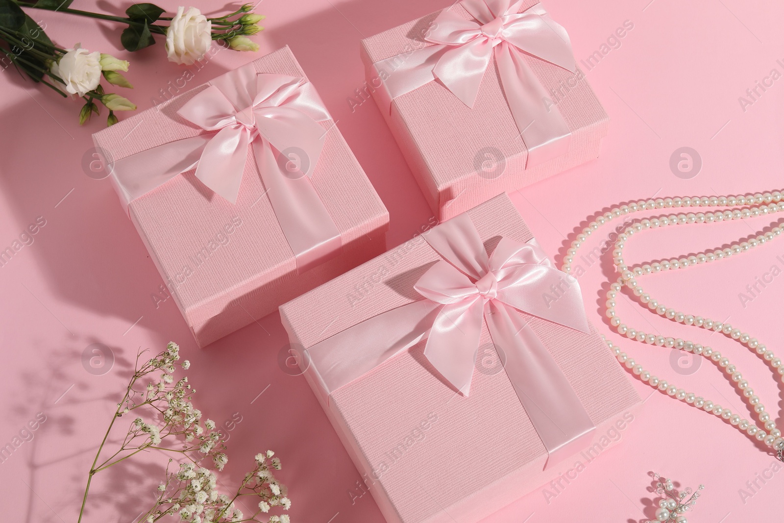 Photo of Beautiful wedding gifts, pearl jewelry and flowers on pink background, above view