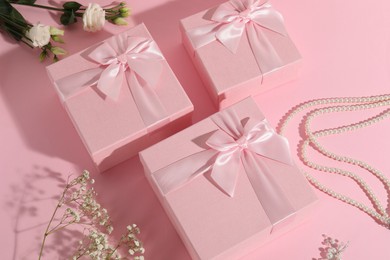 Photo of Beautiful wedding gifts, pearl jewelry and flowers on pink background, above view