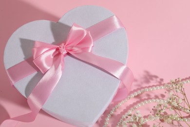 Photo of Beautiful wedding gift, pearl jewelry and gypsophila flowers on pink background, above view