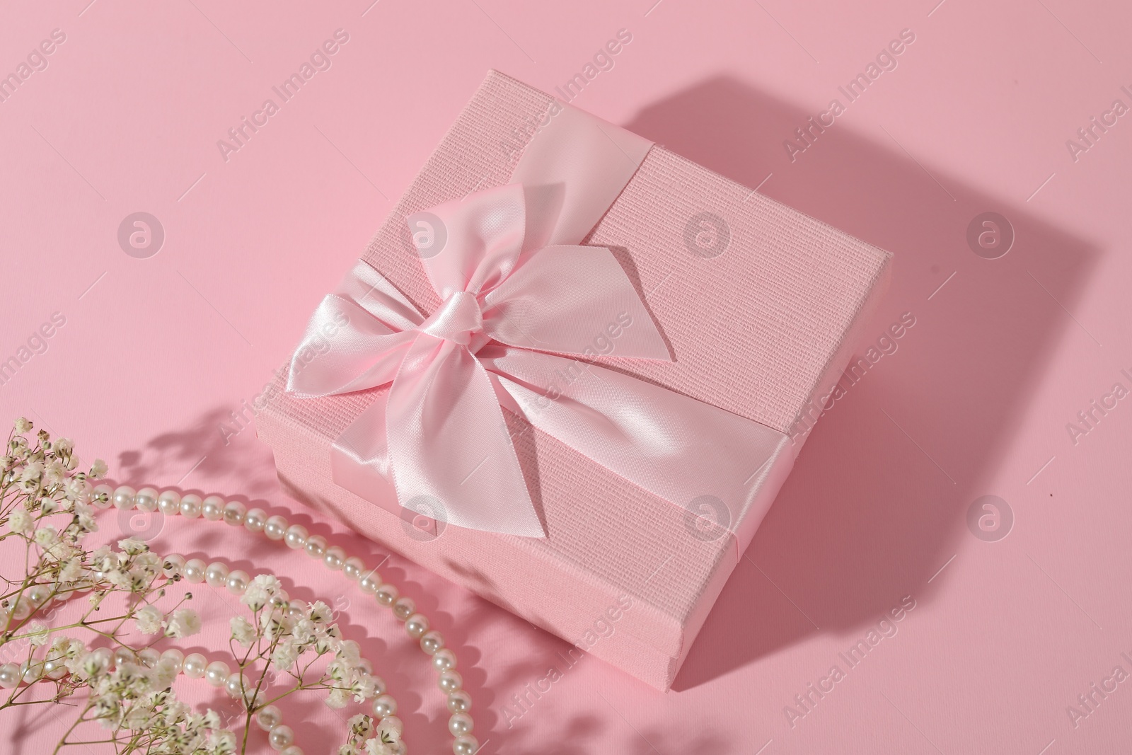 Photo of Beautiful wedding gift, pearl jewelry and gypsophila flowers on pink background, above view