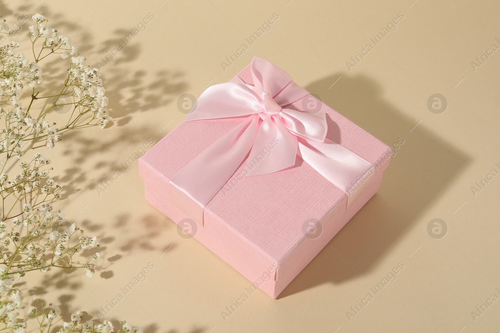 Photo of Beautiful wedding gift and gypsophila flowers on beige background