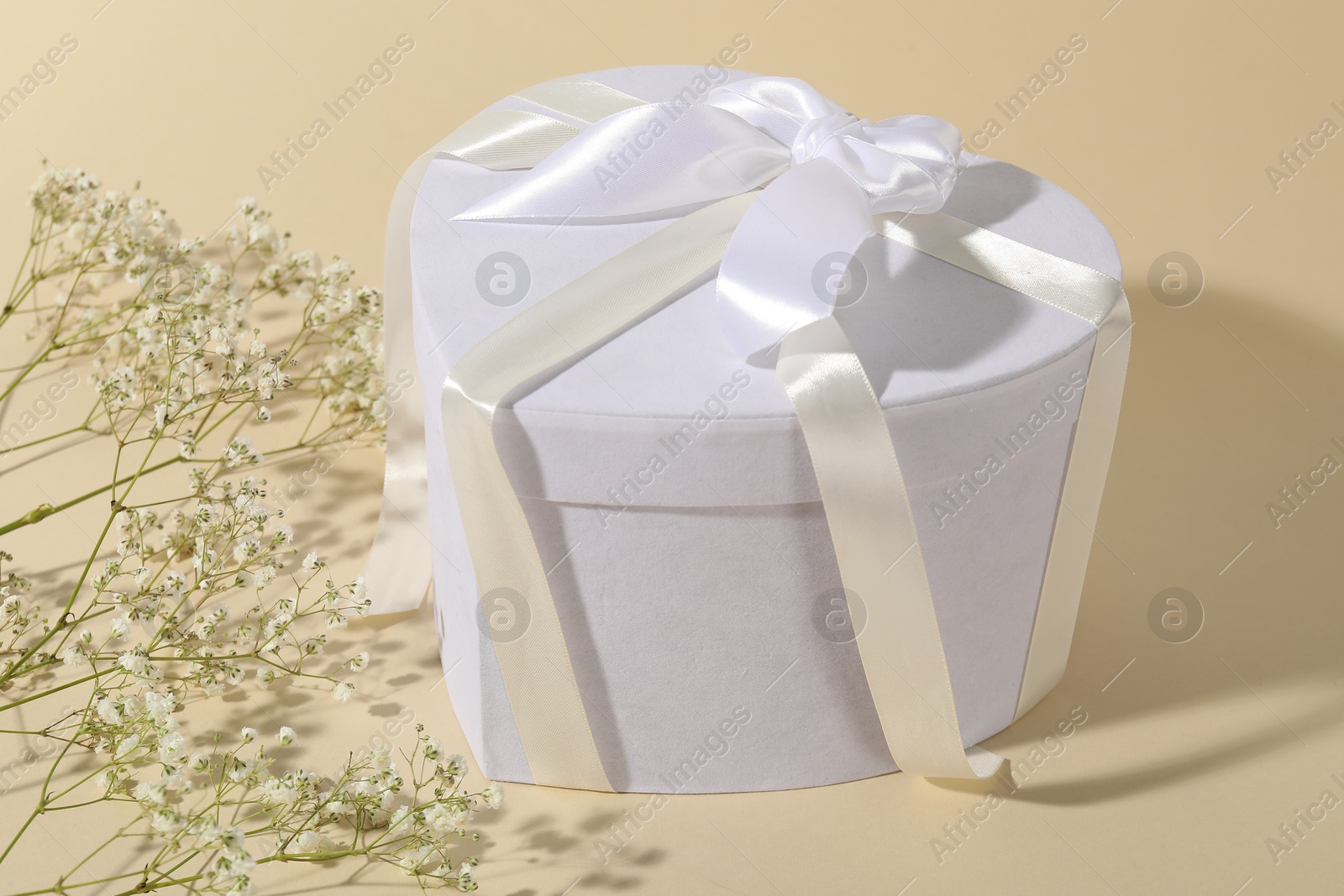 Photo of Beautiful wedding gift and gypsophila flowers on beige background, closeup