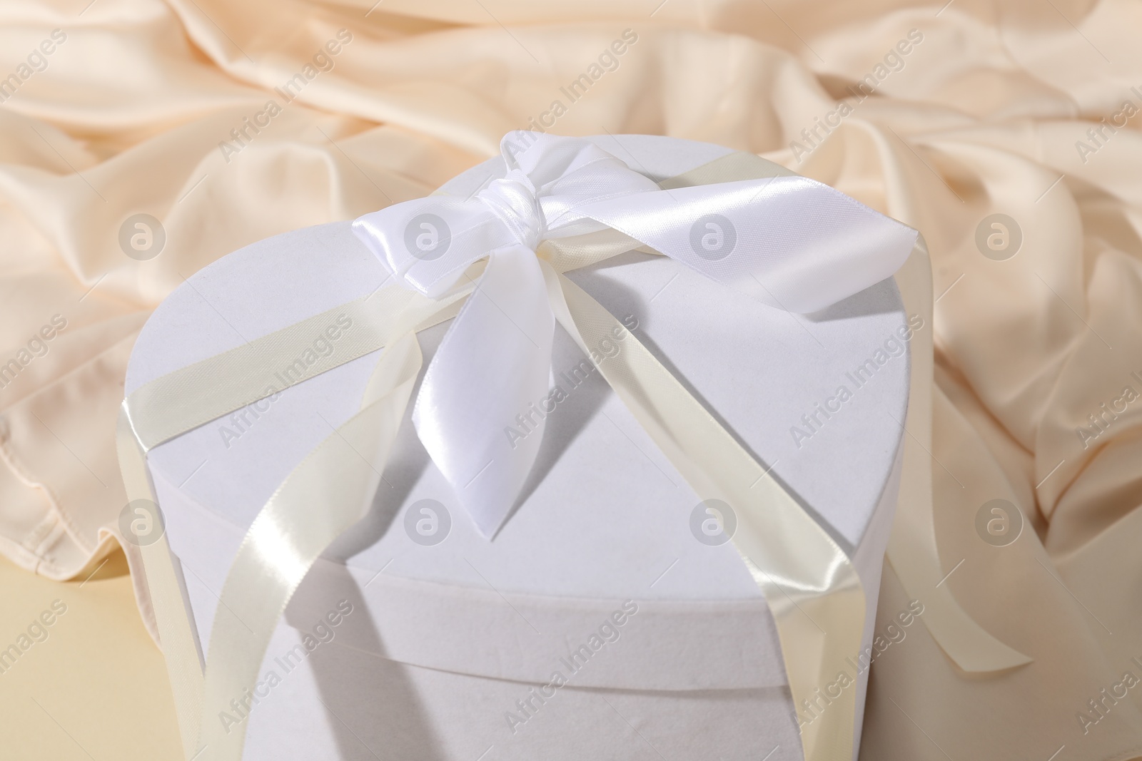 Photo of Beautiful wedding gift and silk fabric on beige background, closeup