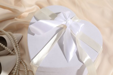 Photo of Beautiful wedding gift, bridal shoes and pearl jewelry on silk fabric, closeup