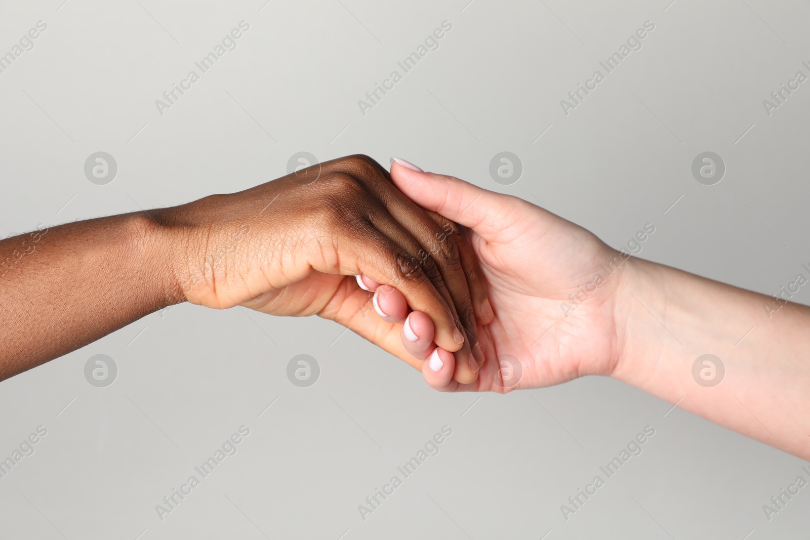 Photo of Stop racism. People of different skin colors holding hands on light grey background, closeup