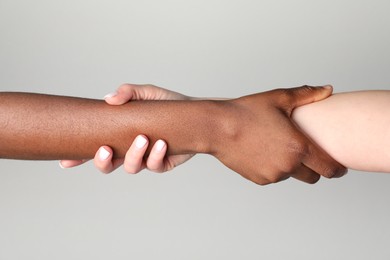 Photo of Stop racism. People of different skin colors holding hands on light grey background, closeup