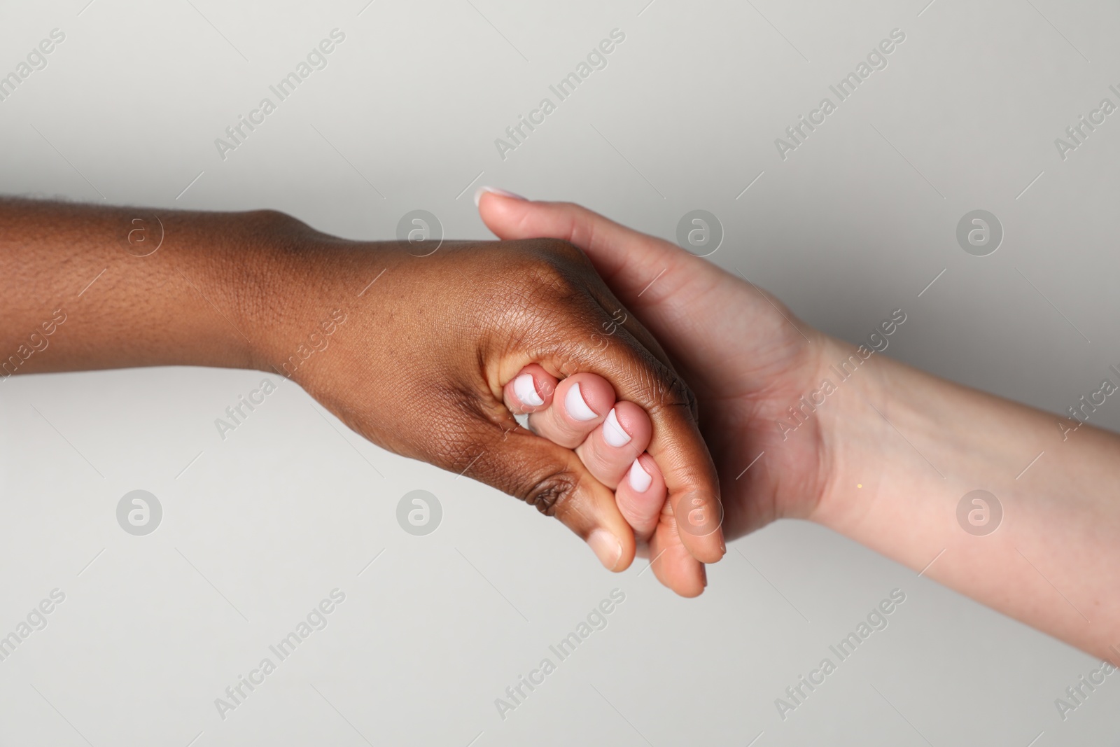 Photo of Stop racism. People of different skin colors holding hands on light grey background, closeup