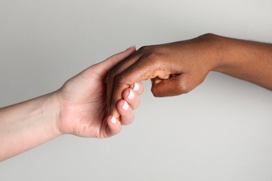 Photo of Stop racism. People of different skin colors holding hands on light grey background, closeup