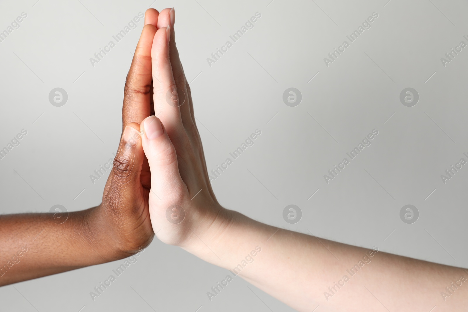 Photo of Stop racism. People of different skin colors giving high five on light grey background, closeup. Space for text