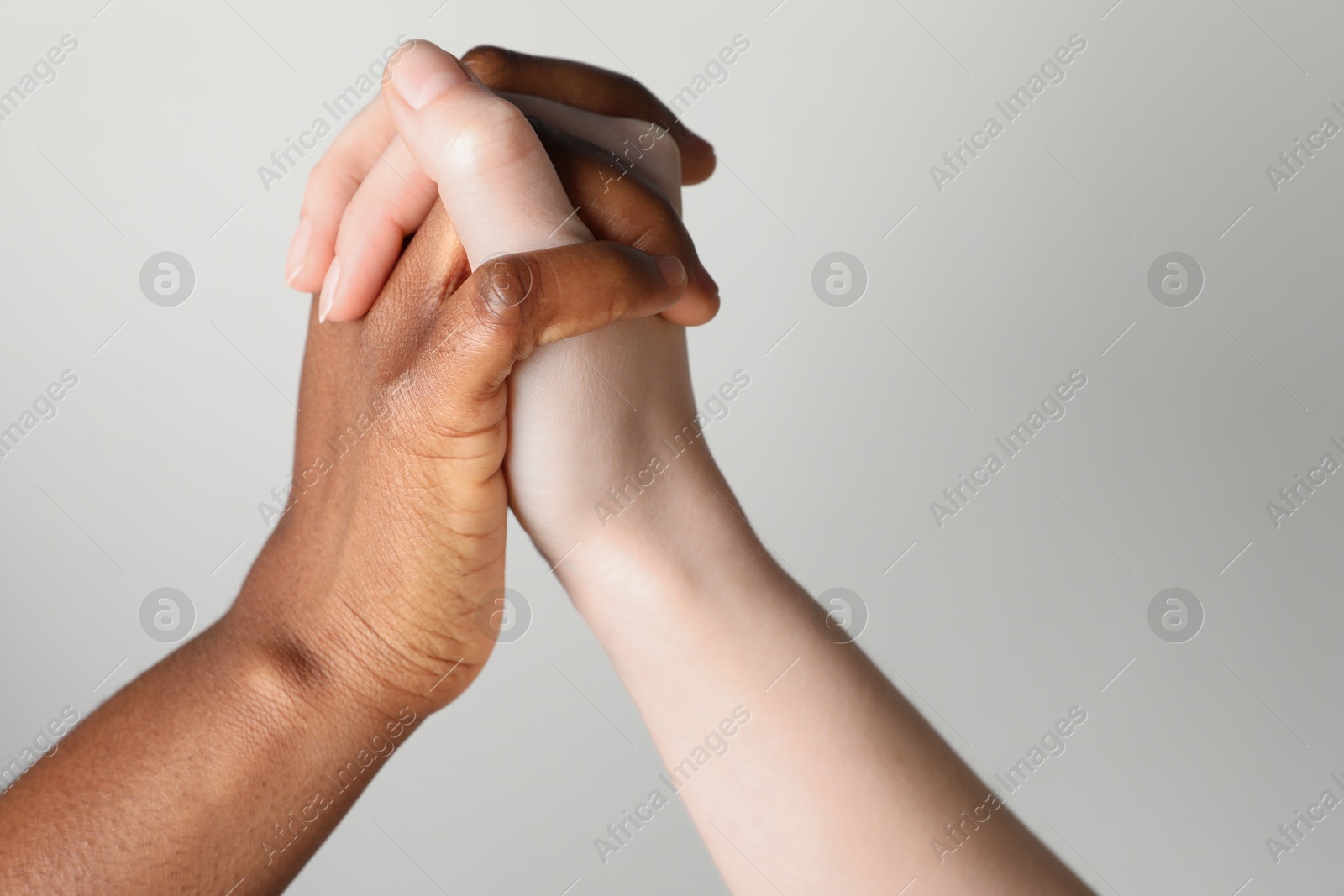 Photo of Stop racism. People of different skin colors holding hands on light grey background, closeup. Space for text