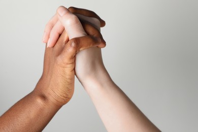 Photo of Stop racism. People of different skin colors holding hands on light grey background, closeup. Space for text