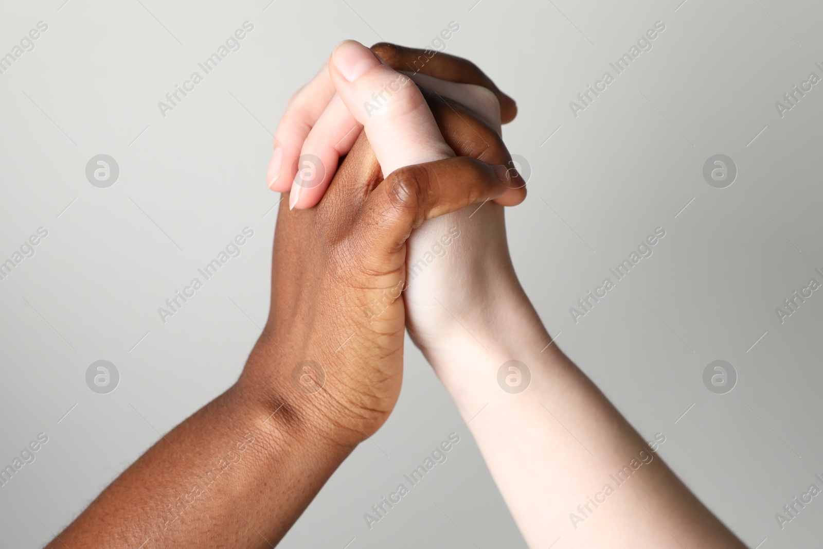 Photo of Stop racism. People of different skin colors holding hands on light grey background, closeup