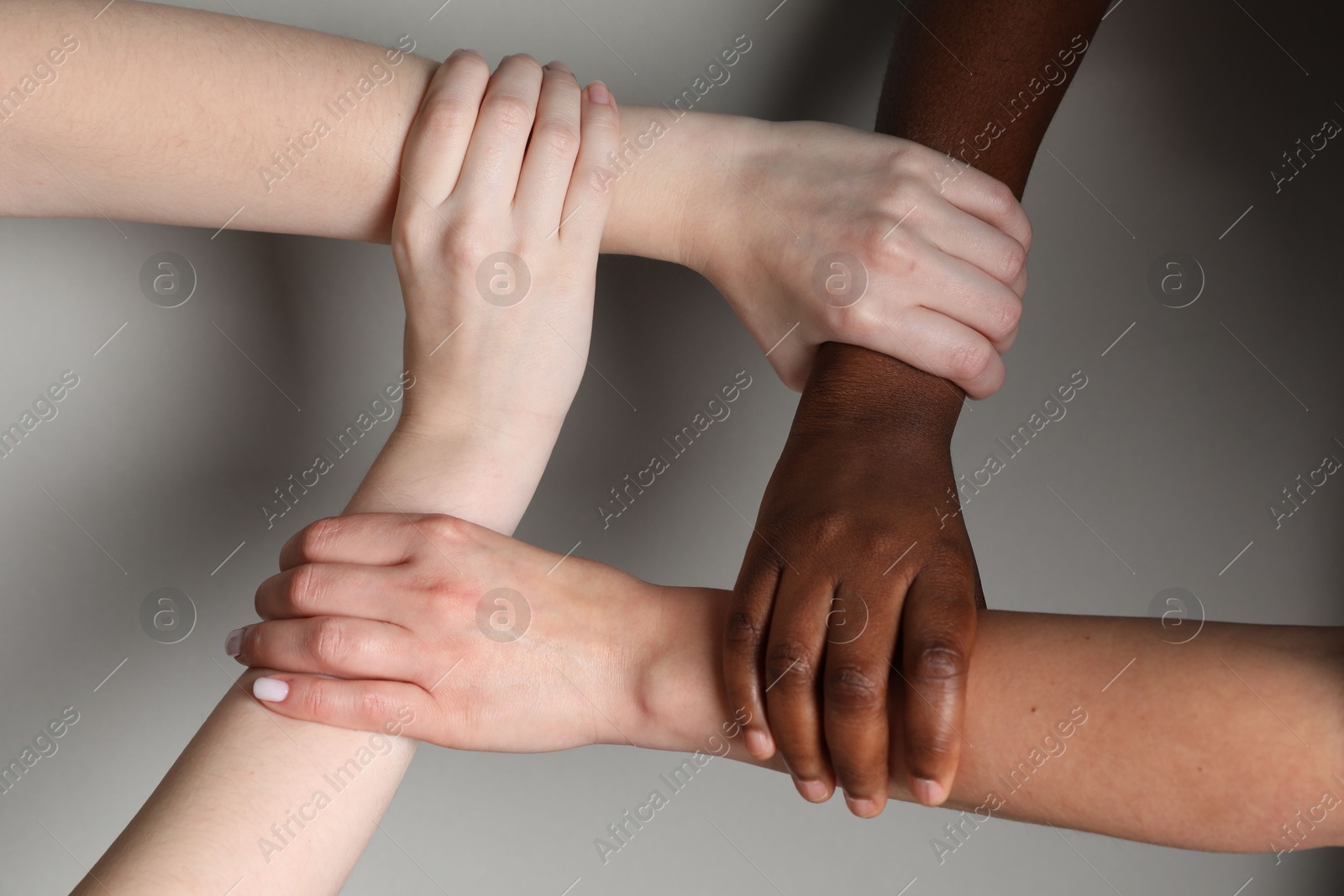 Photo of Stop racism. People of different skin colors joining hands on light grey background, closeup