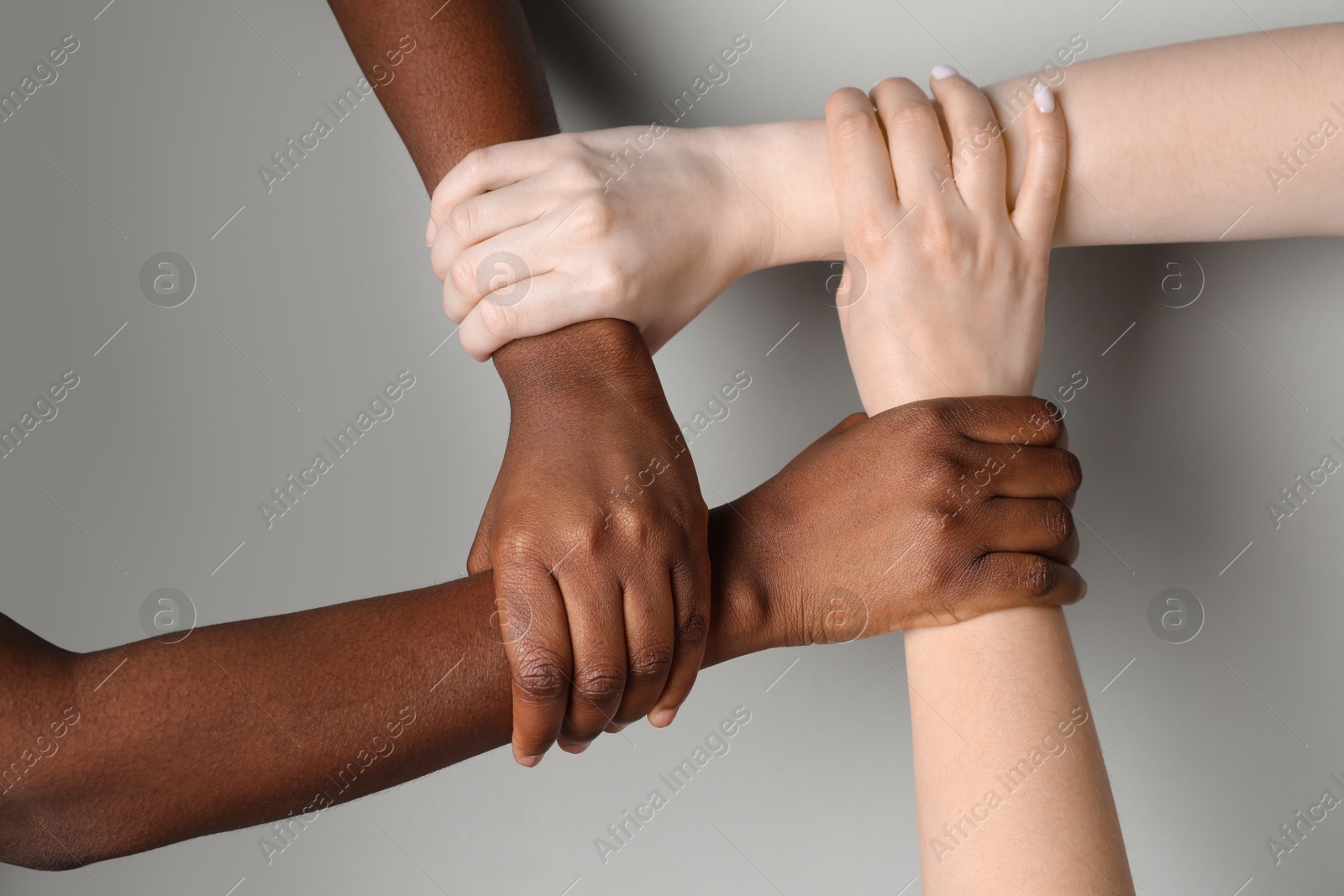 Photo of Stop racism. People of different skin colors joining hands on light grey background, closeup