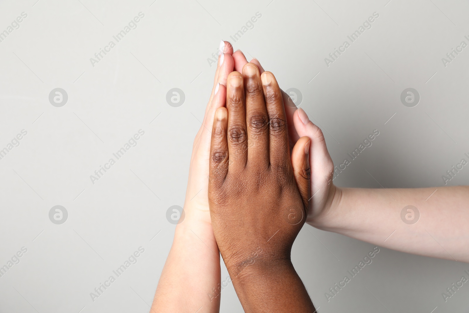 Photo of Stop racism. People of different skin colors joining hands on light grey background, closeup