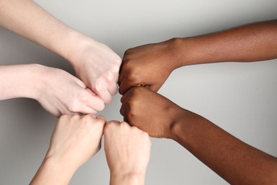 Photo of Stop racism. People of different skin colors bumping fists on light grey background, closeup