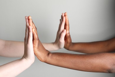 Photo of Stop racism. People of different skin colors joining hands on light grey background, closeup