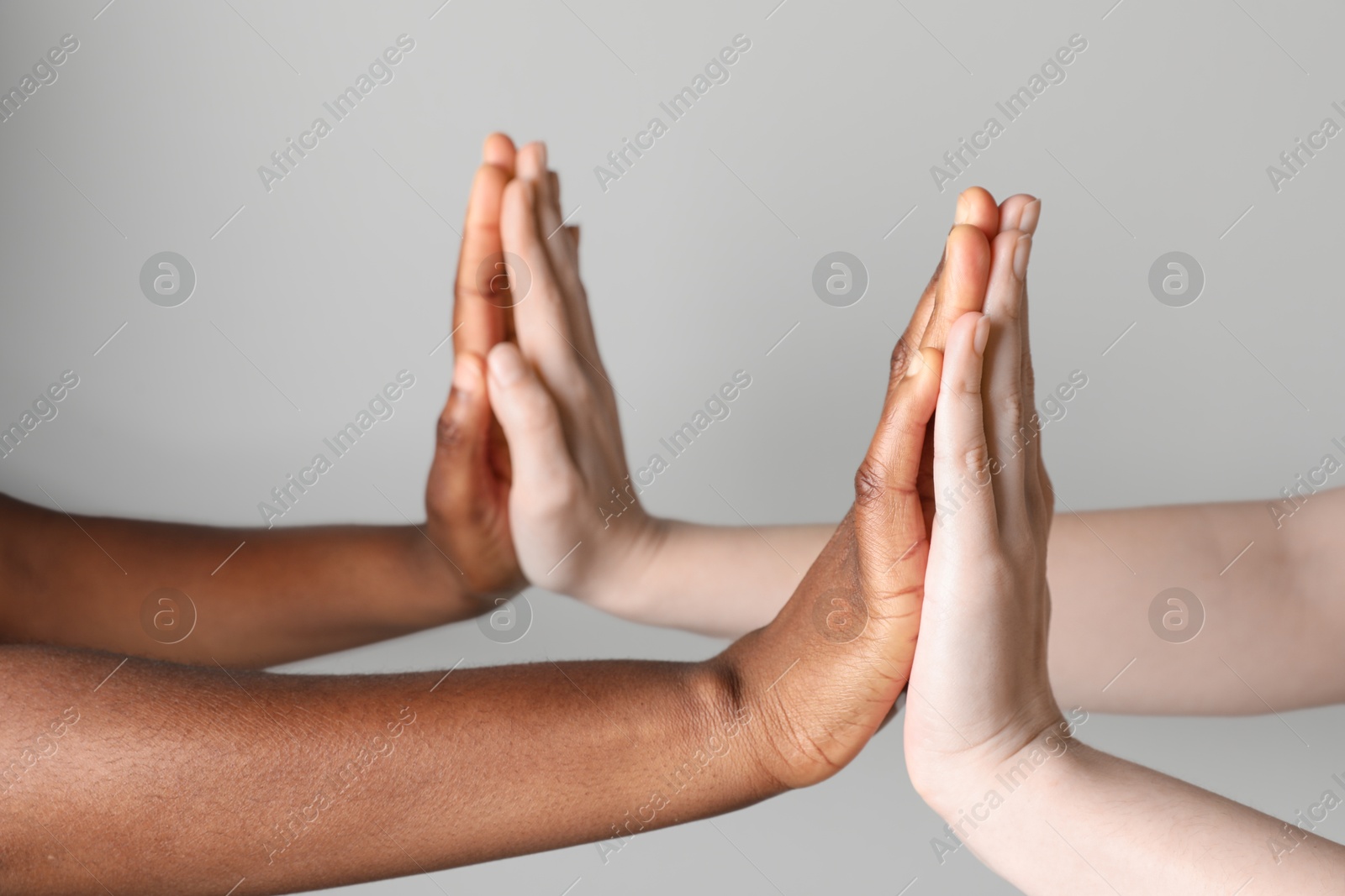 Photo of Stop racism. People of different skin colors joining hands on light grey background, closeup