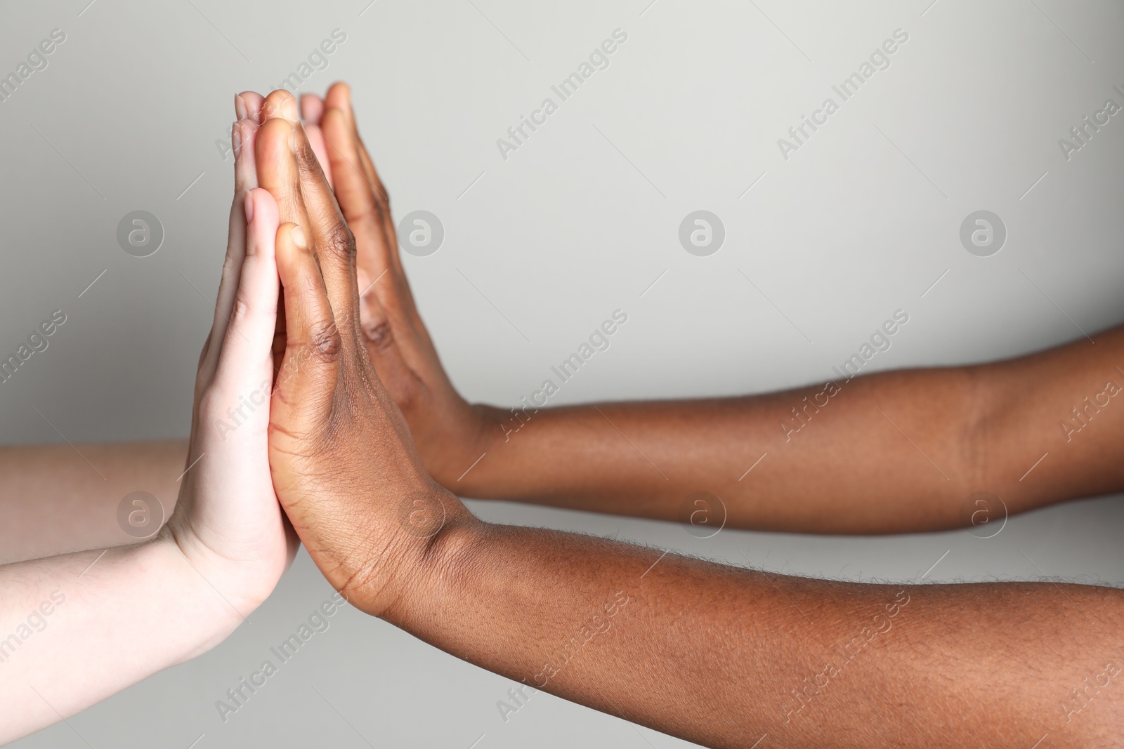 Photo of Stop racism. People of different skin colors joining hands on light grey background, closeup